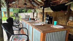 Een buitengedeelte met een bar, een houten toonbank, metalen stoelen en een rustieke houten achtergrond.