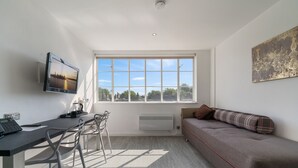 Una habitación moderna y bien iluminada con un gran ventanal, un televisor de pantalla plana, un sofá y una zona de comedor con sillas.