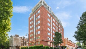 Un edificio de varios pisos de ladrillo rojo con entrada en esquina, ventanas grandes y techo plano.