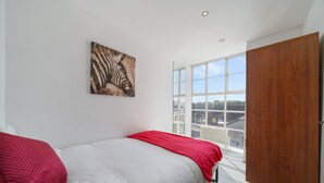 Een slaapkamer met een groot raam, een zwart-wit zebra schilderij en een rode sprei.