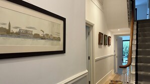 A hallway with a framed cityscape artwork, a patterned carpet, and a staircase with a wooden handrail. - Contemprary central London 5 bed townhouse (London)