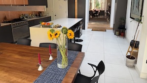 A modern kitchen with a central island, pendant lights, and a dining area with a vase of sunflowers. - Contemprary central London 5 bed townhouse (London)