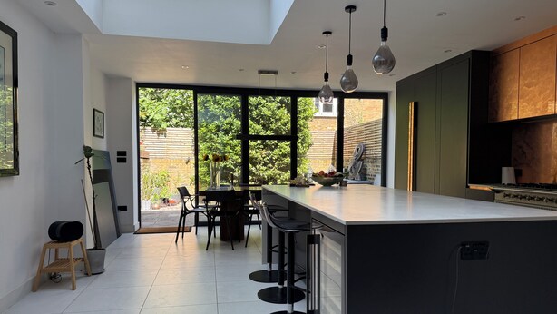 A modern kitchen with a large island, bar stools, and a view of the garden through large windows. - Contemprary central London 5 bed townhouse (London)
