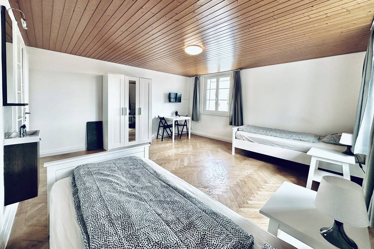 A room with a bed, a desk, a chair, a TV, and a window with curtains.