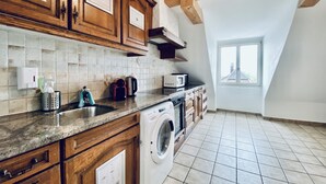 A kitchen with wooden cabinets, a washing machine, and a microwave. - ZIMMERzuVERMIETEN.ch Flumenthal SO (Flumenthal)