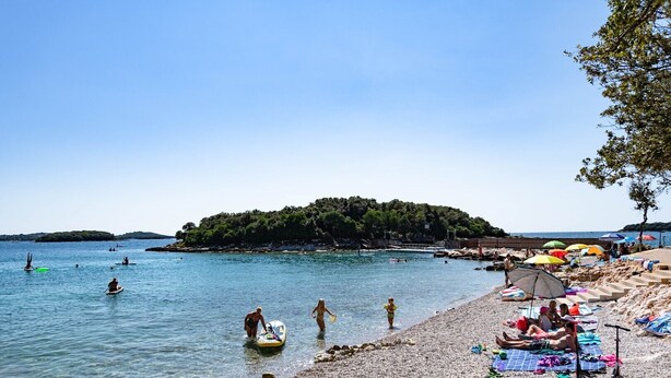 A beach with clear water, people swimming and sunbathing, and a small island in the background. - Casa Riccardo Premium Holday Home (Funtana)