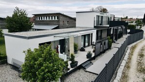 Un edificio residencial moderno con techo plano, ventanas grandes y un espacio al aire libre pavimentado con plantas en macetas.