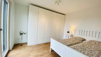 A bedroom with a bed, a wardrobe, a bedside table with a lamp, and a view of the outdoors.