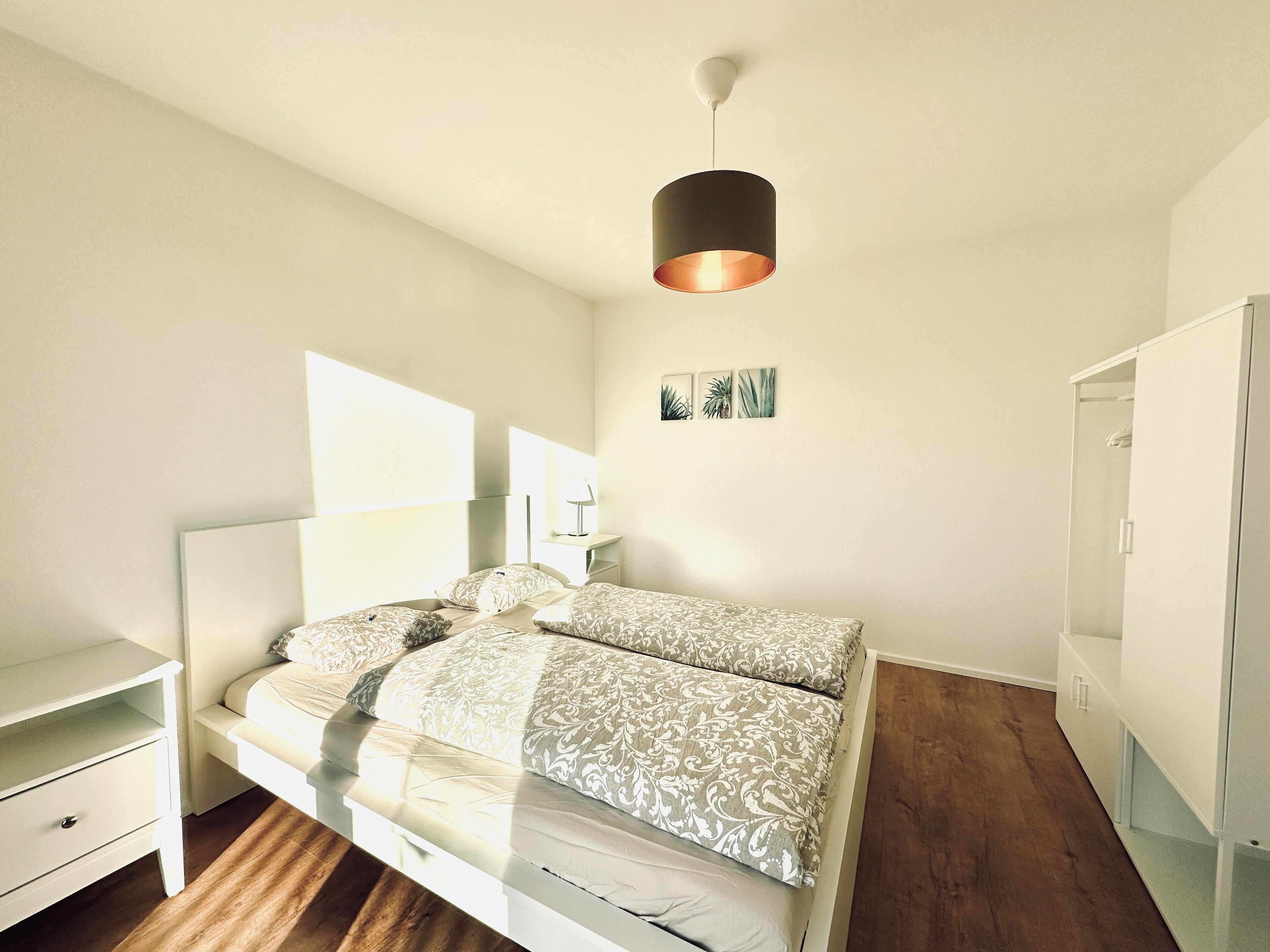 A bedroom with a bed, bedside tables, a wardrobe, and a hanging light fixture.