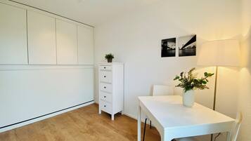 Une pièce moderne et minimaliste, avec une table blanche, un meuble blanc et un lampadaire. Deux tableaux encadrés ornent le mur.