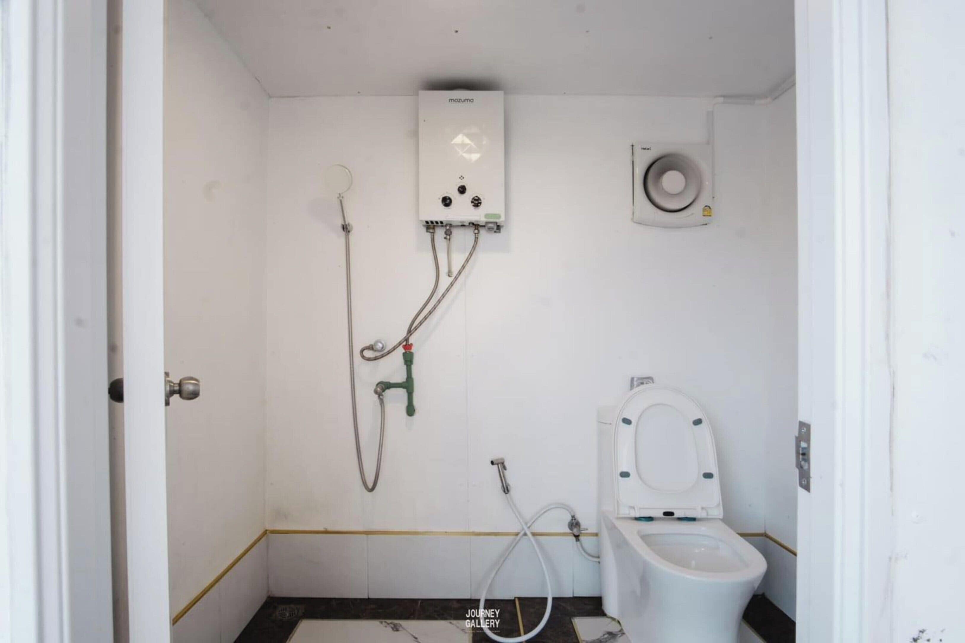 A small, basic bathroom with a toilet, a shower, and a water heater.