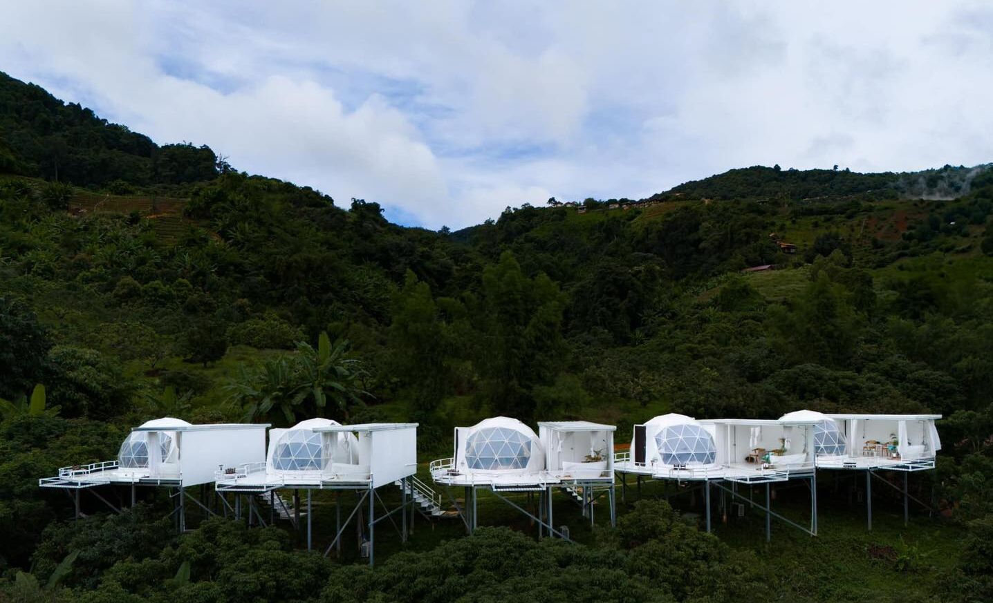 A series of dome-shaped structures elevated on stilts, surrounded by lush greenery and hills.