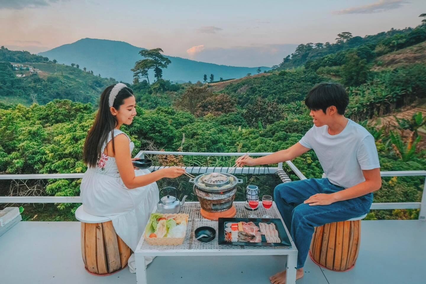 Deux personnes sont assises à une table, devant un paysage verdoyant, avec un barbecue et une variété de plats à portée de main.