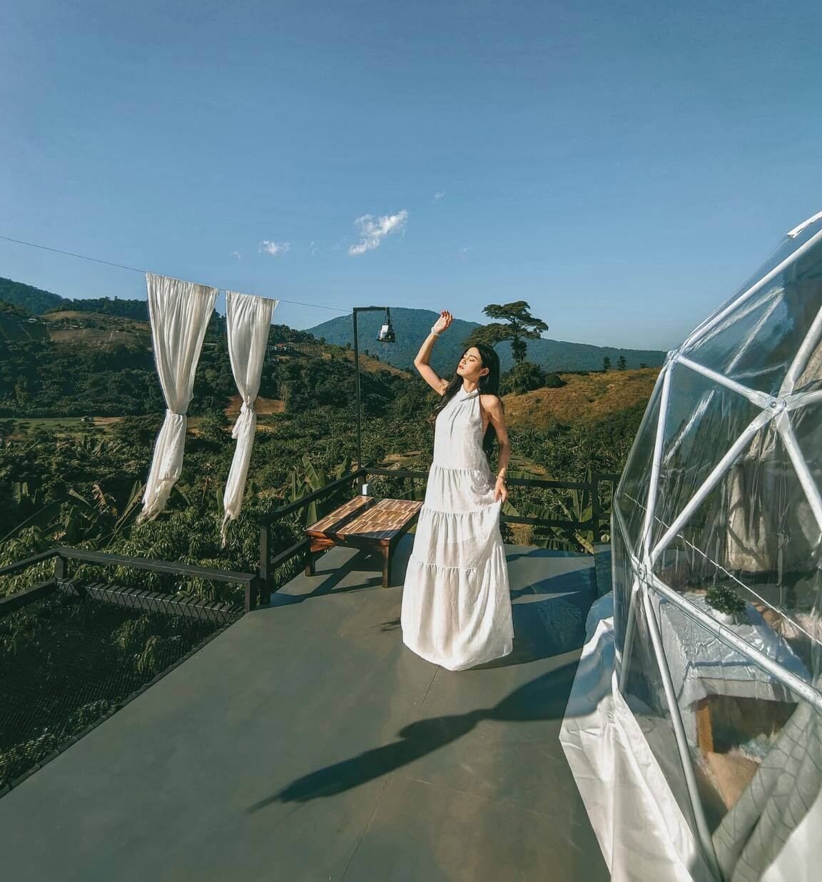 A person standing on a balcony with a view of a hilly landscape.