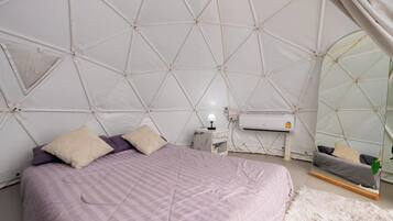 Ett sovrum med ett geometriskt mönster i taket, en säng med ett lila överkast, ett sängbord med en lampa och en spegel som reflekterar sängen.