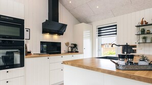 A modern kitchen with white cabinetry, a wooden countertop, and a black range hood. - 5 Star Holiday Home in Hadsund (Hadsund)