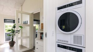 A laundry room with a stacked washer and dryer, wooden flooring, and a potted plant. - 5 Star Holiday Home in Hadsund (Hadsund)