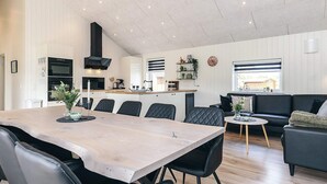 A modern kitchen with a central island, a dining area with a large table and chairs, and a living area with a sofa and a small coffee table. - 5 Star Holiday Home in Hadsund (Hadsund)