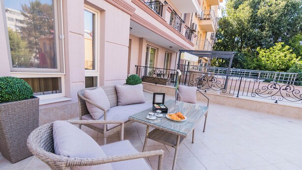 Un área de estar al aire libre con mobiliario de mimbre, una mesa con un croissant y vistas a un edificio con balcones.