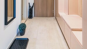 Un pasillo con una puerta de madera, una planta en maceta, un felpudo negro y un banco.