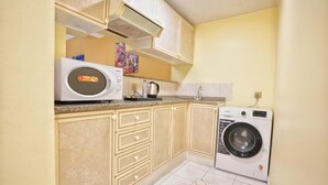 A compact kitchen with a microwave, a washing machine, and a coffee maker. - Imperiaa by HOC Globe (Dubai)