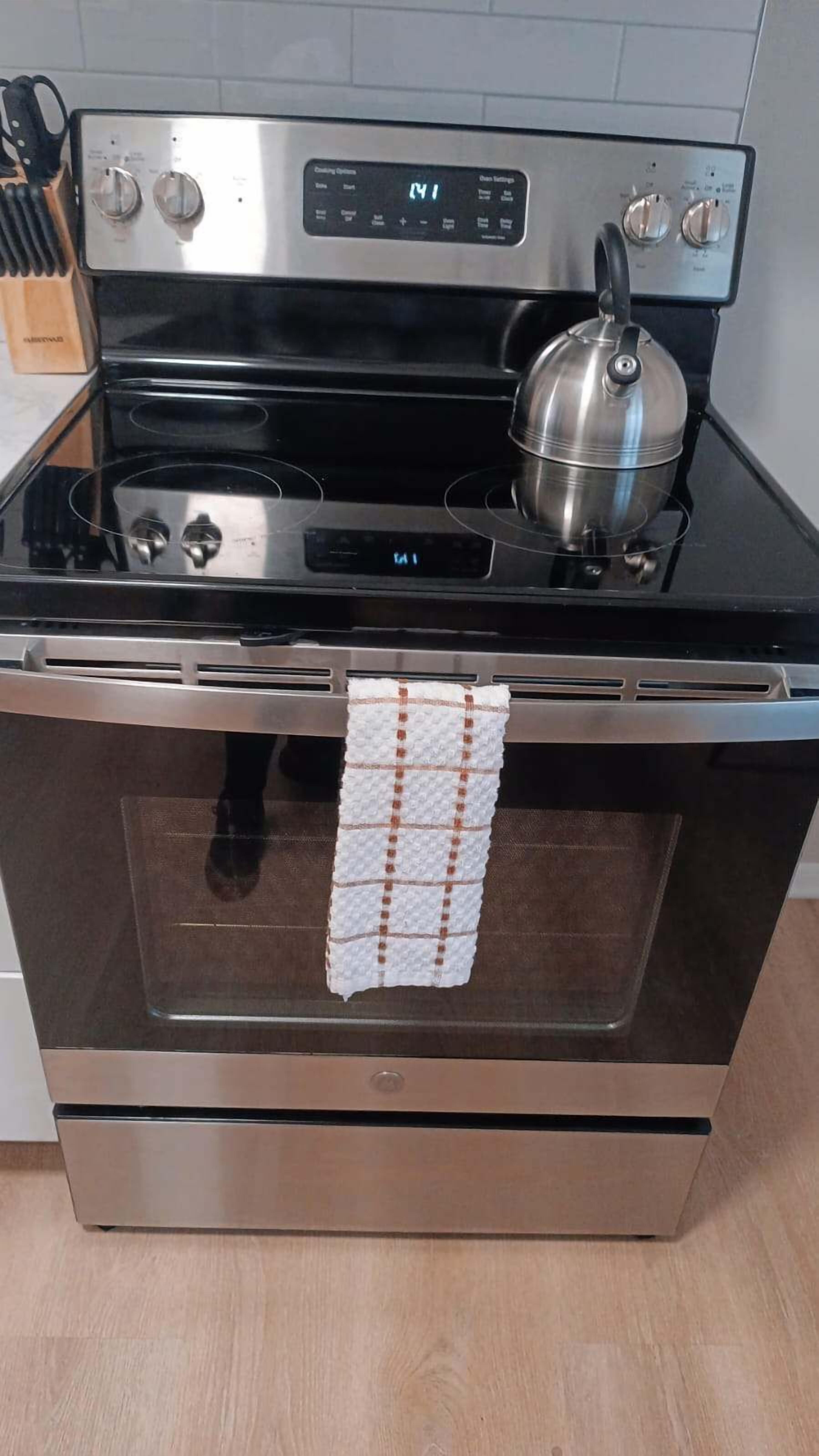 A stainless steel oven with a digital control panel, a kettle, and a checkered towel hanging inside.