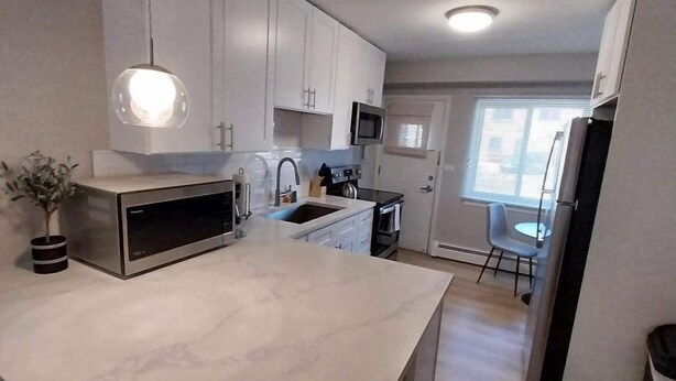Una cocina moderna con armarios blancos, una isla grande, microondas y un comedor con una silla y mesa.