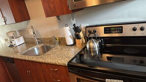 Una cocina con estufa de acero inoxidable, encimera de granito, armarios de madera, un hervidor y una cafetera.