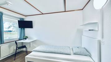 Una habitación con cama, escritorio, silla, televisión y ventana con cortinas.