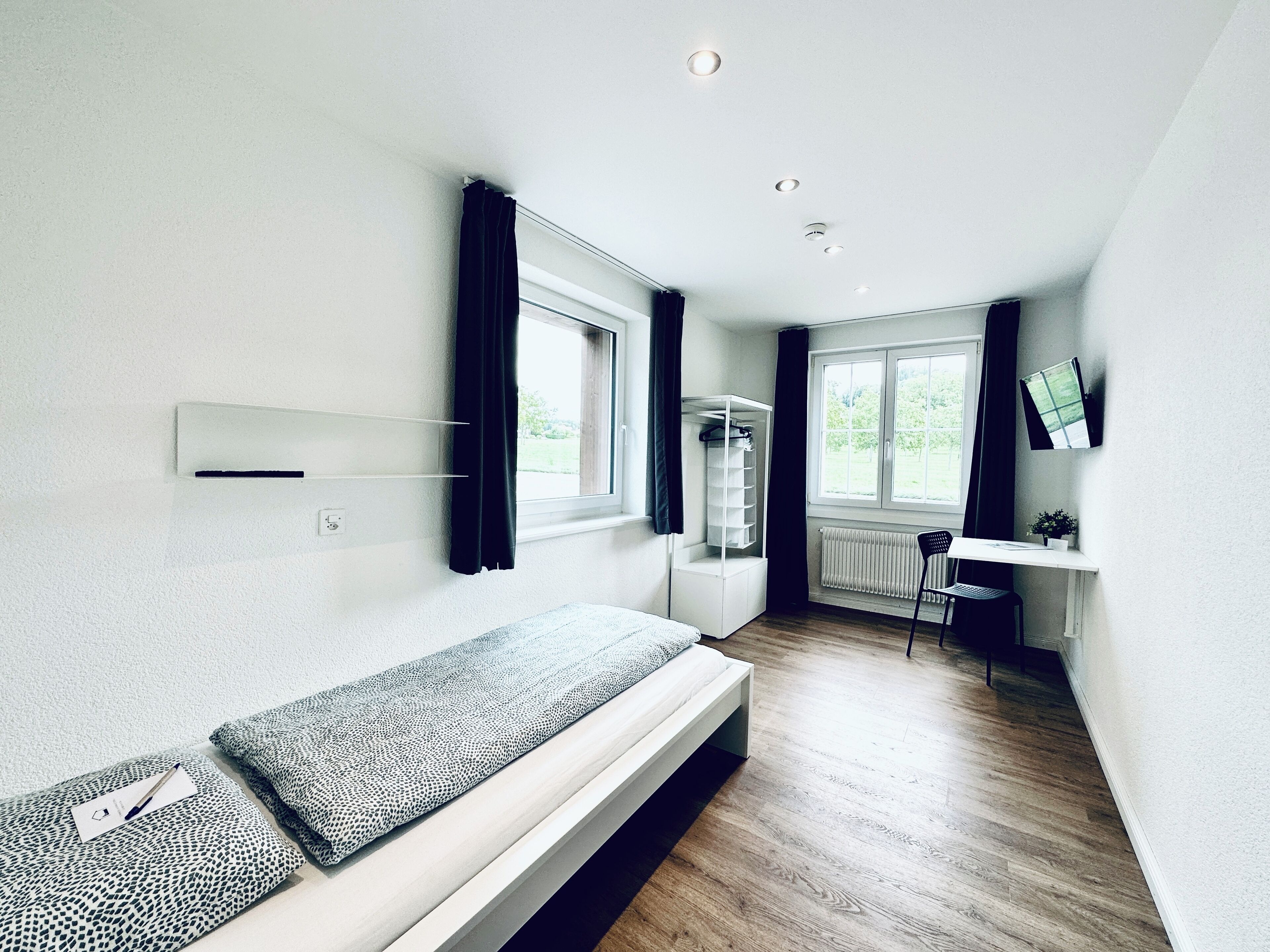 A compact, modern room with a bed, a desk, and a window.