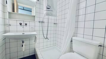 Un baño con lavamanos, inodoro y ducha blancos. Hay una toalla colgada en la cortina de la ducha.