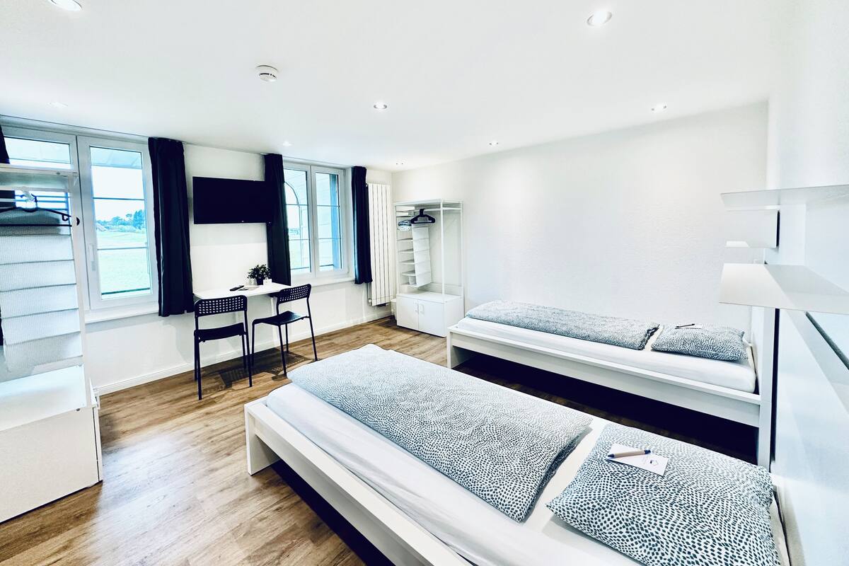 Een moderne, minimalistische slaapkamer met een bed, bureau en garderobe.