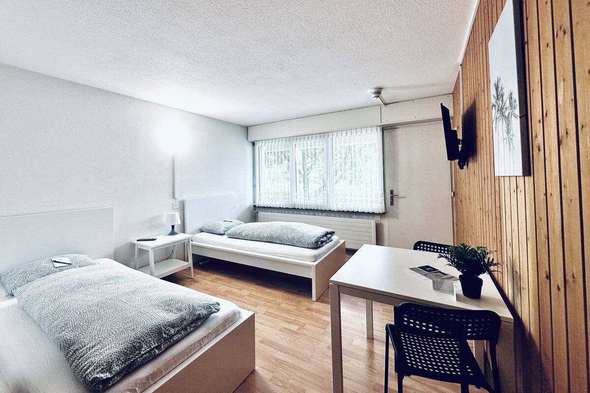 Een kleine kamer met een bed, nachtkastje en een klein bureau met stoel.