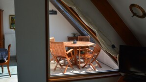A dining area with a round wooden table and chairs, a television, and a window with a view of the outside.