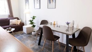 A modern living room with a sofa, a coffee table, a dining table with chairs, a floor lamp, and wall art. - Levanda Syros with Free Parking (Ermoupoli)
