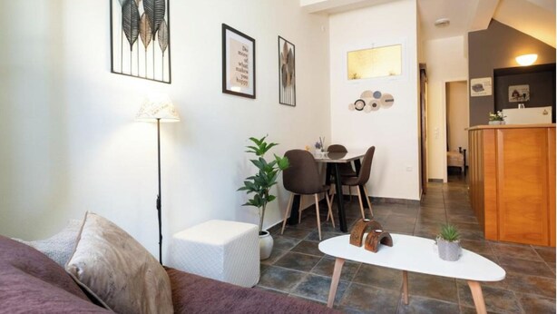 A modern living room with a sofa, a coffee table, and a dining area with chairs and a table. There are framed pictures on the walls and a small plant on the coffee table. - Levanda Syros with Free Parking (Ermoupoli)