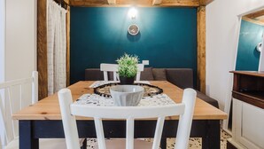 A dining area with a wooden table, white chairs, a potted plant, and a blue wall with a clock. - Oceano & Mare Apartments  (Trapani)