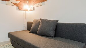 A gray sofa with two pillows against a white wall, a wooden ceiling with a light fixture, and a power outlet on the wall. - Oceano & Mare Apartments  (Trapani)