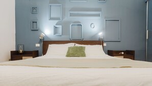 A neatly made bed with a wooden headboard, white linens, and a green throw pillow. There are two bedside tables with lamps, and the walls are decorated with geometric frames. - Oceano & Mare Apartments  (Trapani)