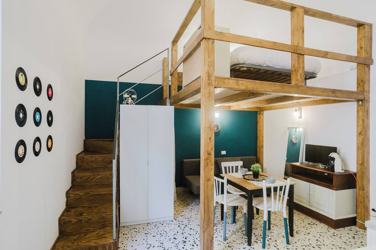 A compact room with a bunk bed, a dining area with a table and chairs, a kitchenette, and a staircase.
