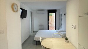 A compact living space with a dining area, a bed, a TV, and a door leading to an outdoor area. - Studio rental (minimum 2 nights). (Béziers)