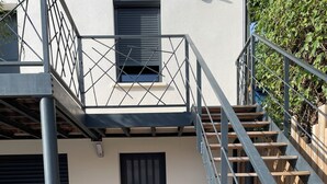 A building with a staircase leading to a wooden deck, a black door, and a metal railing. - Studio rental (minimum 2 nights). (Béziers)