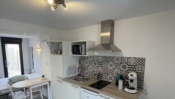 A compact kitchen with a microwave, stove, and sink. There is a dining table with chairs and a small potted plant. - Studio rental (minimum 2 nights). (Béziers)