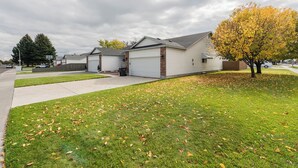 A residential area with houses, a driveway, and a lawn with fallen leaves. - Welcome to Mountain Getaway in this cozy 4 bed 3 bath home. (Idaho Falls)