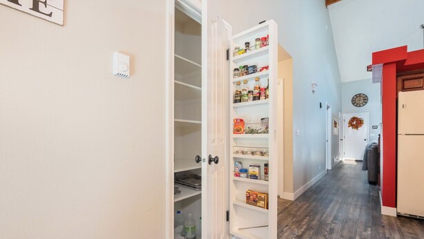 A hallway with a white pantry door open, revealing shelves stocked with food items. - Welcome to Mountain Getaway in this cozy 4 bed 3 bath home. (Idaho Falls)