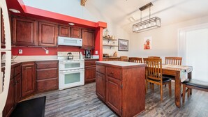 A compact kitchen with wooden cabinets, a white stove, and a dining area with wooden chairs and a table. - Welcome to Mountain Getaway in this cozy 4 bed 3 bath home. (Idaho Falls)
