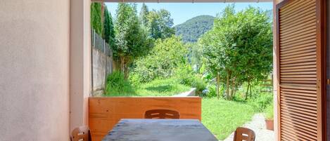 A covered outdoor dining area with a table and chairs, a view of a green landscape with trees and hills.