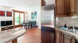 Cucina con frigorifero in acciaio inox, mobili in legno, piano di lavoro in granito e zona pranzo con sedie e tavolo.