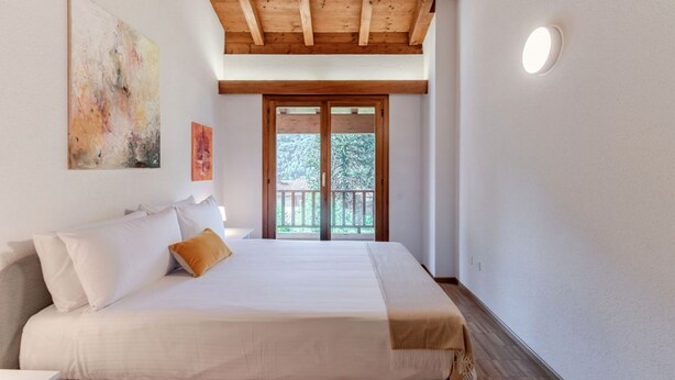 Una camera da letto con un letto, soffitto in legno, una porta finestra e un quadro appeso al muro.