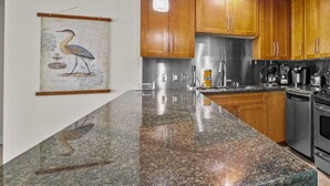 A kitchen with granite countertops, stainless steel appliances, wooden cabinets, and a framed artwork on the wall. - Ocean Club 408 | Enjoy Views of the Gulf! (Biloxi)